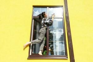 un mujer a mano lavados el ventana de el casa con un trapo con un rociar limpiador y un fregona afuera. la seguridad a altura, restaurar orden y limpieza en el primavera, limpieza Servicio foto