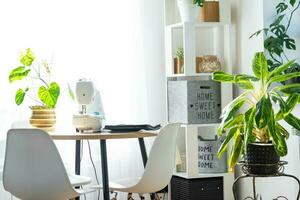 Sewing machine on a round table in the white interior of the house near the window with a transparent curtain, and a home plant in a pot - a modern interior. hobby, home business photo