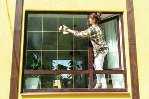 A woman manually washes the window of the house with a rag with a spray cleaner and a mop outside. Safety at height, restoring order and cleanliness in the spring, cleaning service photo