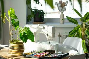 Sewing machine on a round table in the white interior of the house near the window with a transparent curtain, and a home plant in a pot - a modern interior. hobby, home business photo