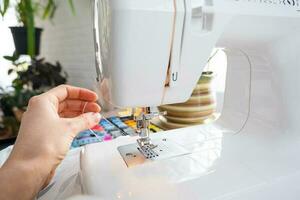 Woman hand close up sews tulle on electric sewing machine. Filling the thread into the sewing needle, adjusting the tension. Comfort in the house, a housewife's hobby, layout of sewing tools photo