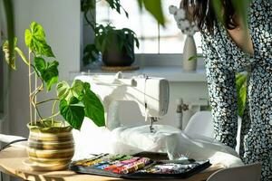 un mujer cose tul en un eléctrico de coser máquina en un blanco moderno interior de un casa con grande ventanas, casa plantas. comodidad en el casa, un ama de casa pasatiempo foto