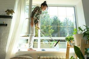 mujer a mano lavados el ventana de el casa con un trapo con rociar limpiador y fregona dentro el interior con blanco cortinas restaurar orden y limpieza en el primavera, limpieza servise foto