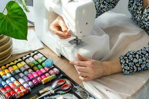 Woman hand close up sews tulle on electric sewing machine. Filling the thread into the sewing needle, adjusting the tension. Comfort in the house, a housewife's hobby, layout of sewing tools photo