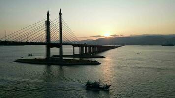 A fishing boat is move at sea near Penang Bridge in sunrise morning video