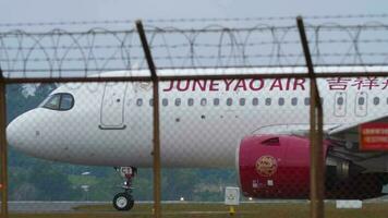 PHUKET, THAILAND JANUARY 28, 2023 - Airbus A320 of Juneyao Airlines taxiing at Phuket Airport. Chinese airline. Passenger plane on the airfield, view through the fence. Tourism travel concept video