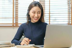 Video call, meeting conference via camera, happy asian young woman, girl sitting, wear headphone study, learn online, using laptop computer or notebook via internet. Freelancer working from home. photo