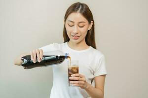 Thirsty, attractive asian young woman, girl holding, pouring cold sparkling water with ice from cola bottle into glass in her hand. Health care, healthy lifestyle concept, isolated on white background photo