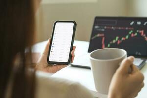 Investor analyzing exchange market, asian young business woman trader on graphic charts on laptop computer, hand in using smartphone for trading stock, looking at screen with diagrams at home office. photo