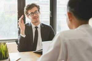 asiático joven gerente, empleador hombre entrevista con persona, tener pregunta acerca de currículum y escucha a candidato respuesta, conversacion juntos a oficina. reclutamiento empleado trabajo concepto. foto