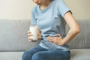 Pain, suffering asian young woman having a stomachache, abdominal pain or digestive, hand in holding belly after drink glass of milk. Lactose intolerance, allergy from dairy food, health care problem. photo