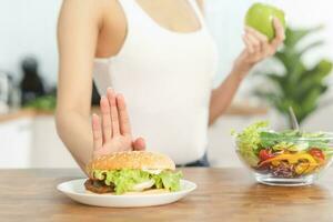 dieta, dieta asiático joven mujer o niña empujar afuera, negar hamburguesa, basura comida y escoger verde manzana, mezcla vegetales ensalada, comer comida para bueno saludable, salud cuando hambriento. hembra peso pérdida gente. foto