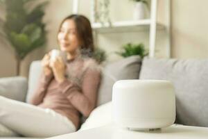 moderno aire humidificador durante relajarse o descansar, contento borroso asiático joven mujer, niña disfrutando aromaterapia vapor olor desde esencial petróleo difusor cómodo en vivo condiciones habitación, apartamento a hogar foto