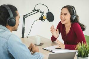 Smile two asian young woman, man radio hosts in headphones, microphone while talk, conversation, recording podcast in broadcasting at studio together. Technology of making record audio concept. photo