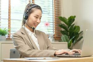 Operator, asian young woman wearing headset, headphones and speaking on video call conference with customer, colleagues support phone, work on laptop computerTechnology of help, consult service photo