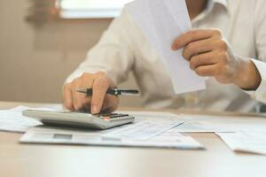 Close up hand of stress asian young businessman, male pressing a calculator to calculate tax income and expenses, bills, credit card for payment or payday at home, office.Financial, finance concept. photo