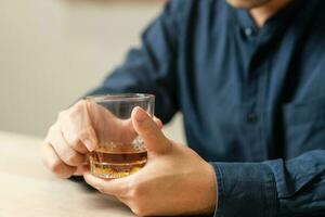 Alcoholism, drunk asian young man, male hand holding a glass of alcohol, whiskey sitting alone, drinking on table at home, at night. Treatment of alcohol addiction, suffer abuse problem alcoholism. photo