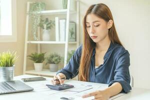 Account finance, asian young business woman hand use calculator for calculate budget, cost and income of company from bills, reports paperwork, plan spend money expenses, working on desk at home. photo