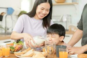 contento refresco familia desayuno en mañana, asiático joven padre padre, madre y pequeño linda chico, niño teniendo comida en cocina comiendo juntos a hogar. alegre, disfrutar Cocinando gente. foto