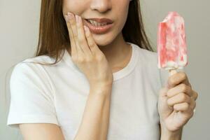 cara expresión sufrimiento desde sensible dientes y frío, asiático joven mujer, niña mano conmovedor su mejilla, sensación herir, dolor comiendo hielo crema, paleta dolor de muelas molar diente a hogar, dental problema. foto