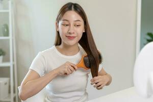 Health hair care, beauty makeup asian woman, girl holding hairbrush and brushing, combing her long straight hair looking at reflection in mirror in morning routine after salon treatment, hairstyle. photo