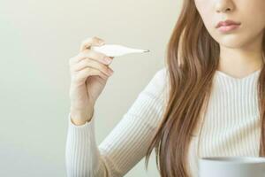 enfermo, influenza asiático joven mujer dolor de cabeza tener fiebre, mano en participación termómetro para cheque medida cuerpo temperatura, sensación enfermedad a hogar. salud cuidado, infección de COVID-19. aislado en antecedentes. foto