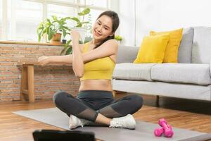 hermosa aptitud asiático joven mujer, niña en ropa de deporte, utilizando tableta para en línea formación fuerza músculos ejercicio, ejercicio formación a hogar para sano cuerpo fuerte atlético adaptar, activo estilo de vida. foto