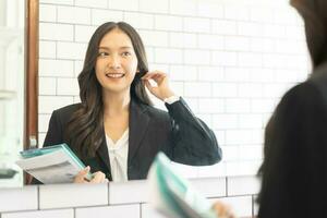 Confident, cheer up asian young woman standing in suit formal, practice talk with look in reflection mirror at toilet before job interview of change career, recruitment employee or staff in corporate. photo