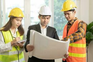 Builder team, asian young engineer man, male and architect woman are discussing construction on blueprint to follow the project to build an industrial plan at site. Engineer worker people concept. photo