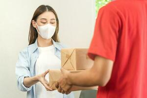 Asian young woman, client received a delivery of cardboard box, parcel from delivery, postman, wearing face mask due to lockdown, quarantine of covid-19 at the door, entrance of her home, house. photo