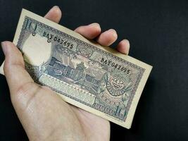 Man holding of old Indonesian banknotes Rp.10,00 issued in 1963. Old rupiah currency concept isolated on a black background. Top view photo