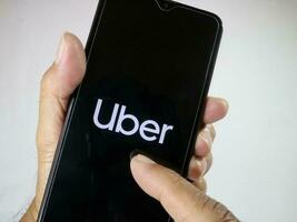 Jakarta, Indonesia, 2023. Hand holding mobile phone with finger touch the Uber logo on screen. photo