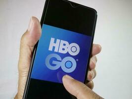 Jakarta, Indonesia, 2023. Hand holding mobile phone with finger touch the HBO Go logo on screen. photo