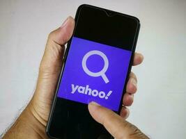 Jakarta, Indonesia, 2023. Hand holding mobile phone with finger touch the Yahoo logo on screen. photo