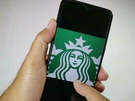 Jakarta, Indonesia, 2023. Hand holding mobile phone with finger touch the Starbucks logo on screen. photo