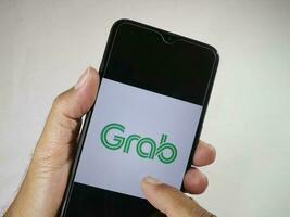 Jakarta, Indonesia, 2023. Hand holding mobile phone with finger touch the Grab logo on screen. photo