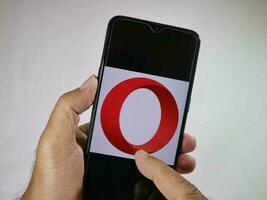 Jakarta, Indonesia, 2023. Hand holding mobile phone with finger touch the Opera logo on screen. photo