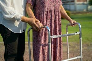 Caregiver help Asian elderly woman patient walk with walker in park, healthy strong medical concept. photo