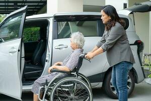 Caregiver help and support asian elderly woman sitting on wheelchair prepare get to her car to travel in holiday. photo