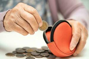 asiático mayor mujer participación contando moneda dinero en cartera. pobreza, ahorro problema en Jubilación. foto