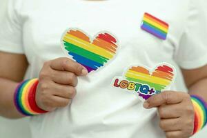 Asian lady wearing rainbow flag wristbands and hold heart, symbol of LGBT pride month celebrate annual in June social of gay, lesbian, bisexual, transgender, human rights. photo