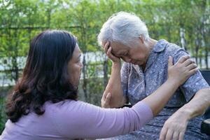 Asian elderly woman headache while sitting on wheelchair at park, healthy strong medical concept. photo