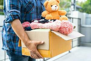 Volunteer woman provide clothing donation box with used clothes and doll to support help for refugee, homeless or poor people in the world. photo