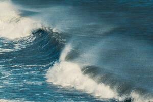 ola azul del océano con salpicaduras golpeando en la playa de arena negra en verano foto