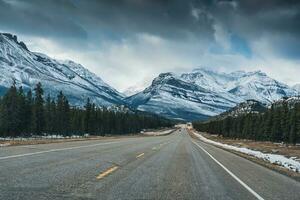 Highway road on the Icefields Parkway with rocky mountains and pine forest in winter photo
