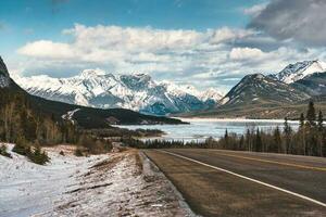 View of highway road into the rocky mountains and frozen lake in Icefields Parkway photo