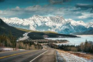 View of highway road into the rocky mountains and frozen lake in Icefields Parkway photo