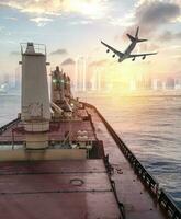 General cargo ship argosy cruising on ocean with plane to urban city at sunrise photo