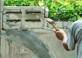 mano de trabajador utilizando martillo imponente y demoler en ladrillo pared a construcción sitio foto