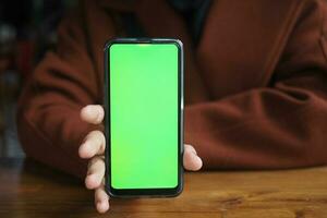 Holding Blank Cell Phone In Hand Showing Green Screen To Camera photo